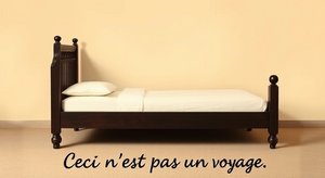 Auf dem Bild ist ein leeres Bett zu sehen mit dem französischen Untertitel "Ceci n'est pas un voyage." (übersetzt: Dies ist keine Reise.). Aufbau und Farbgebung des Bildes ähneln dem berühmten Bild von René Magritte "Ceci n'est pas une pipe." Es wurde generiert mit Künstlicher Intelligenz von DeepAI.